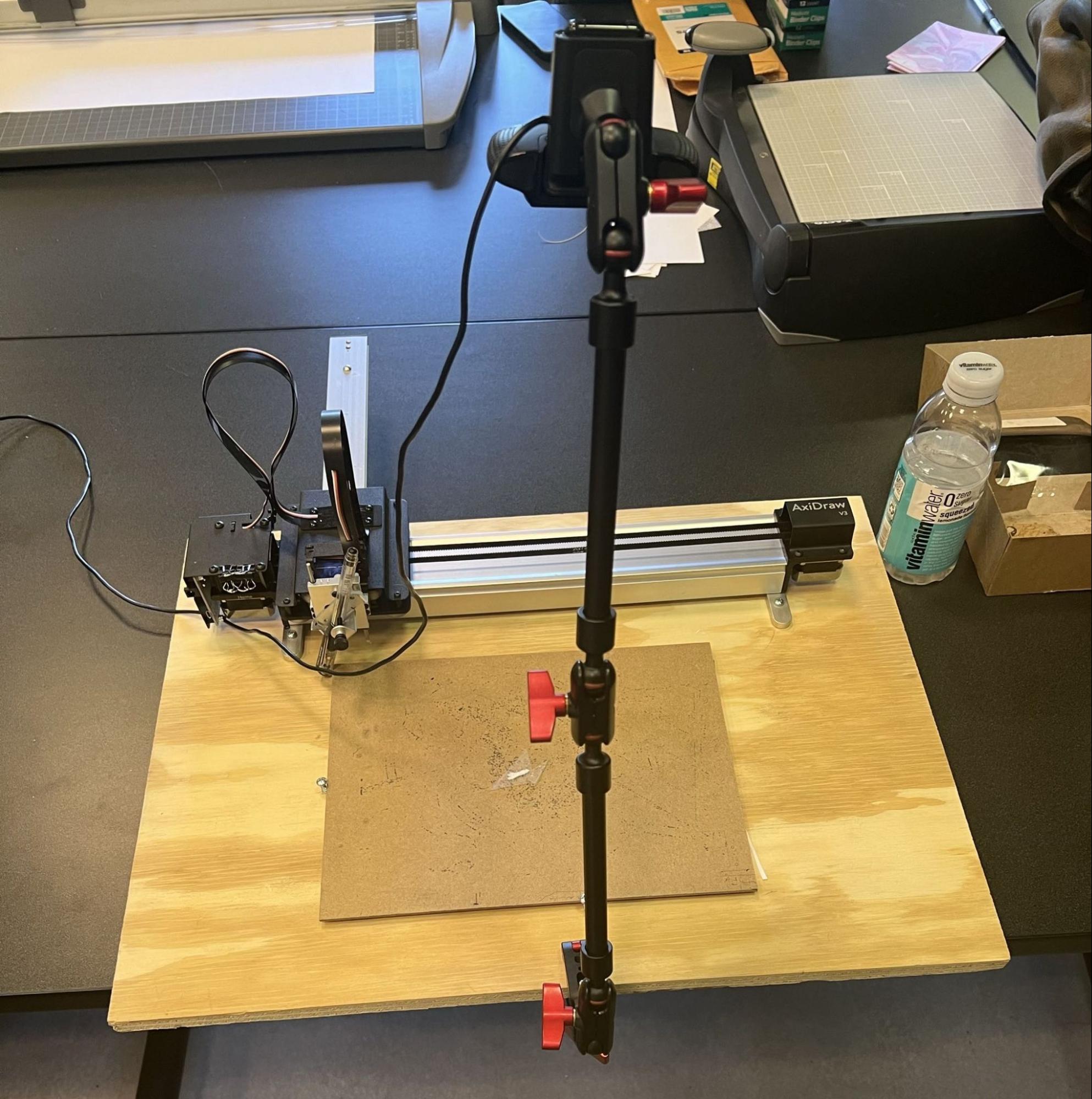 A webcam clamped to an adjustable arm, cantilevered over the Axidraw’s working area