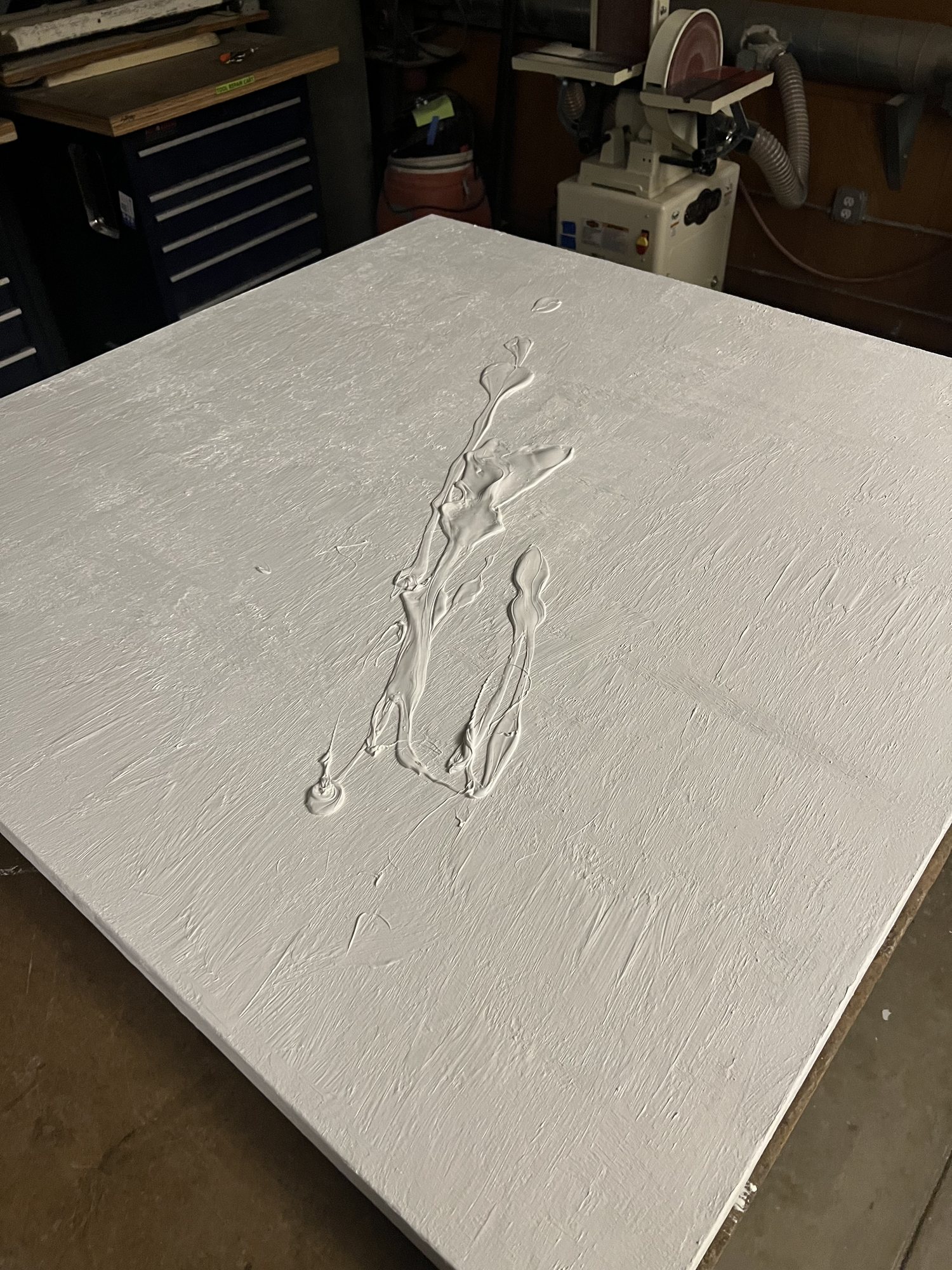 A gessoed canvas on a workshop table, with a raised splatter of gesso across its middle