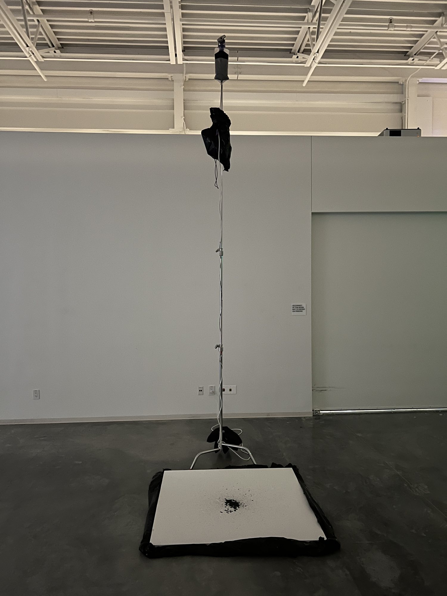 The final installation: a tall stand holds the ink bag and electronics above a white canvas on the floor