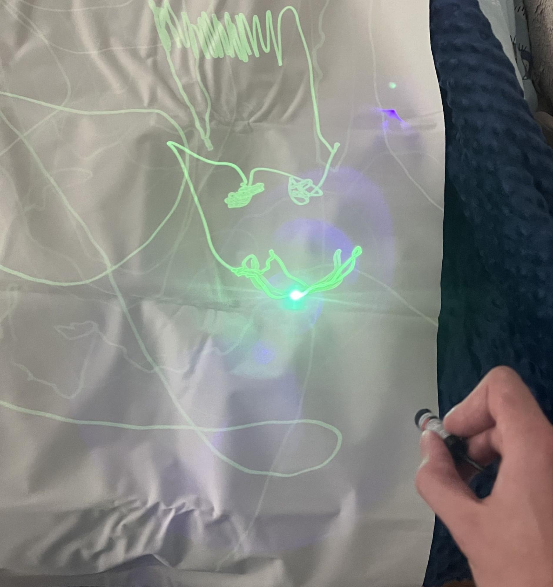 A glowing green line drawn by hand with a laser pointer on phosphorescent fabric, visible in daylight