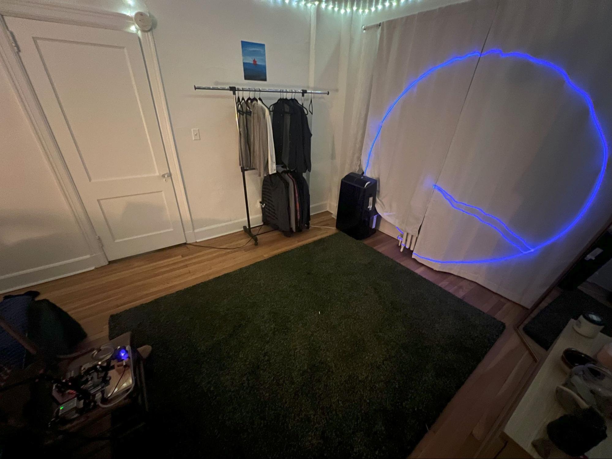 A blue-violet circle projected by the galvo onto a hanging sheet in a bedroom, with a stray line running to its center