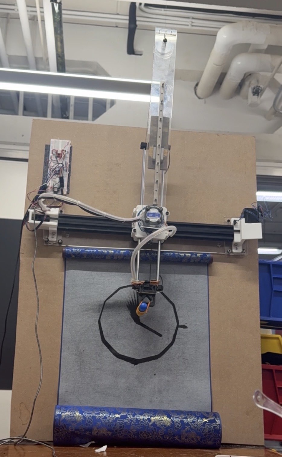 The vertical plotter mounted on the chipboard as a stand-in for the wall, drawing a clock on the cloth